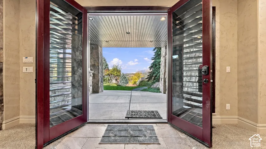 Double entry doors with integrated glass panels, natural stone exterior pillars, recessed ceiling lighting, and concrete patio flooring