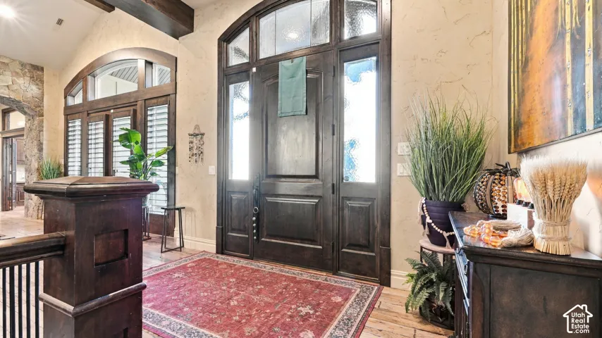 Grand entryway featuring a solid wood door with sidelights, an arched transom window, decorative stone masonry, and exposed timber ceiling beams