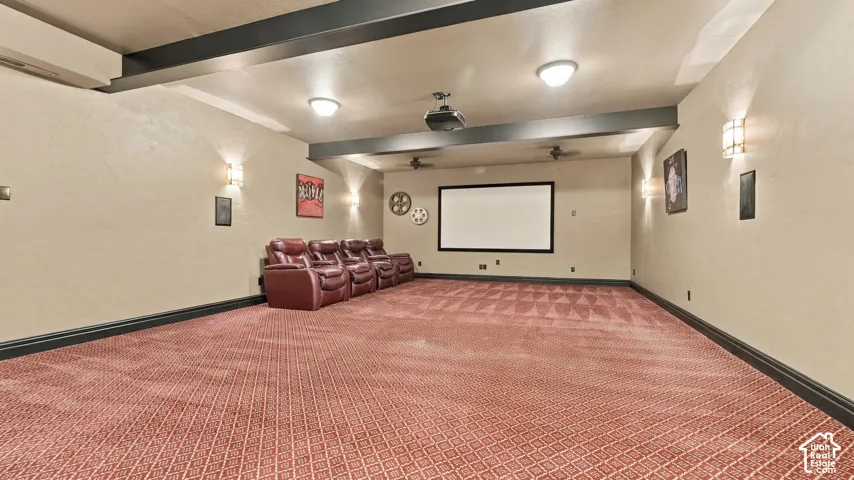 Media room featuring exposed ceiling beams, a mounted projector, a fixed projection screen, and integrated wall sconce lighting