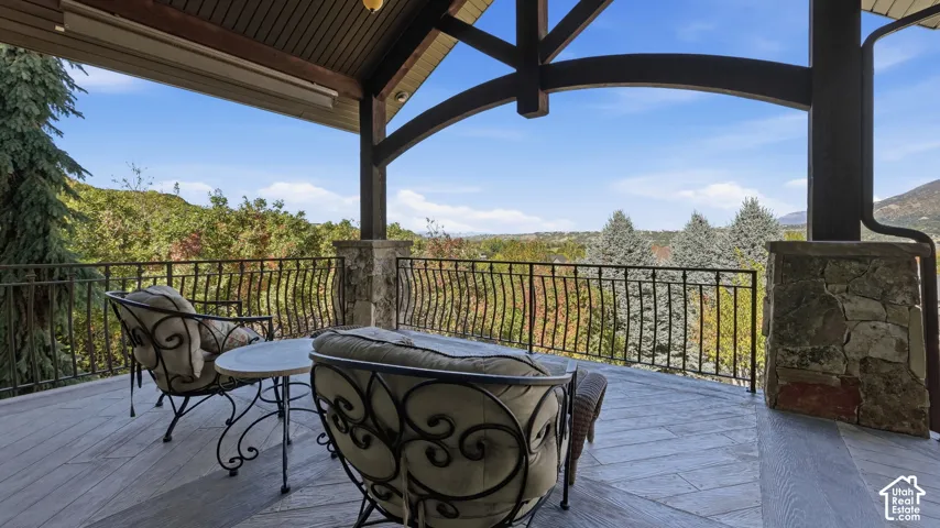 Covered deck featuring wood-finish decking, timber beam architecture, stone masonry columns, and iron railings
