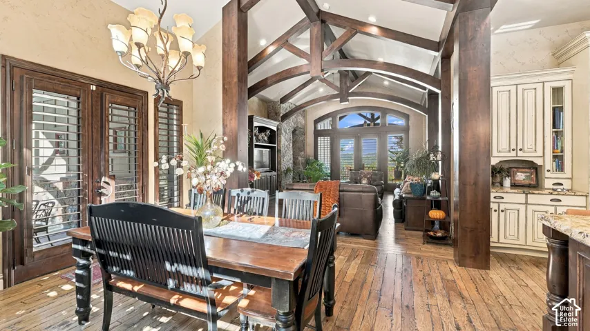 Vaulted ceilings featuring exposed timber trusses, wood-finish flooring, custom built-in cabinetry, and multi-light chandelier
