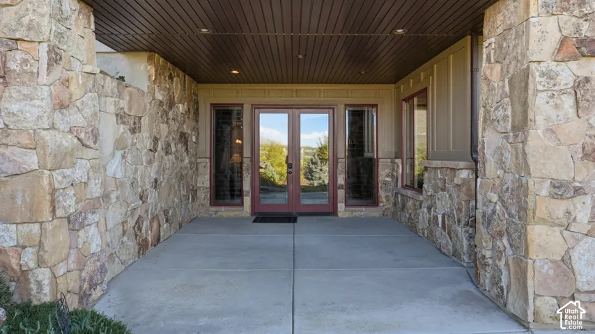 Covered entryway featuring natural stone veneer siding, concrete flooring, double-door entrance, recessed ceiling lighting, and wood-finish soffit