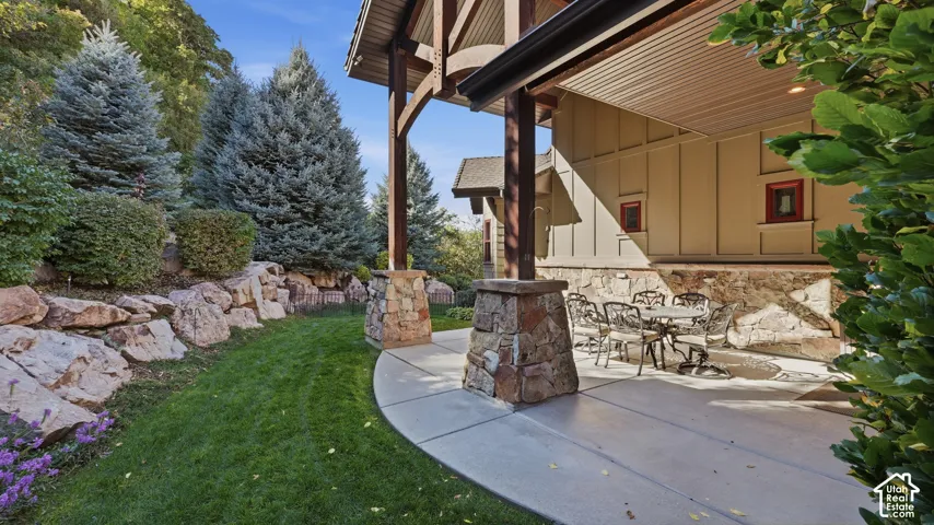 Covered patio featuring stone-clad support columns, board and batten siding, and natural rock landscaping