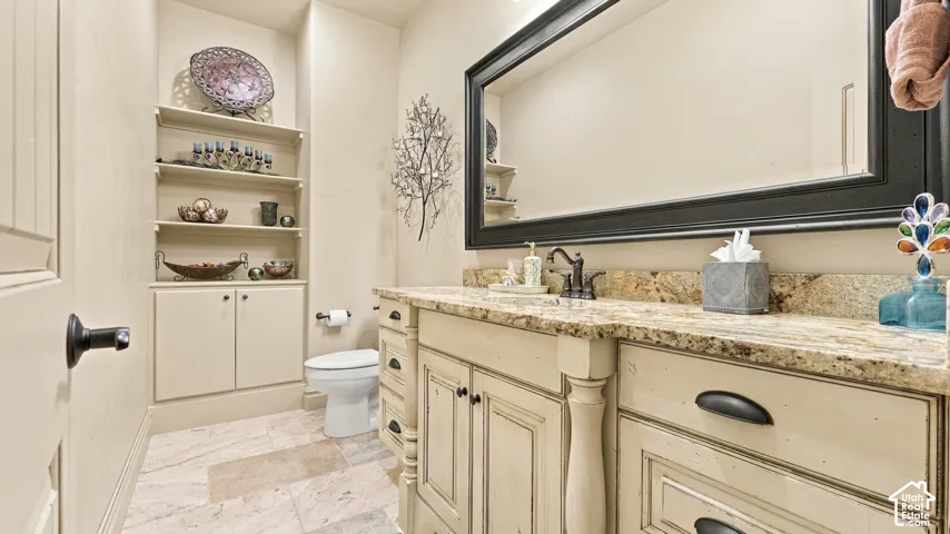 Bathroom featuring a custom vanity with stone-style countertop, integrated sink with oil-rubbed bronze faucet, extensive built-in cabinetry with open shelving, and natural stone flooring