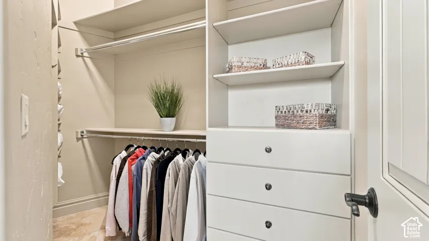 Walk-in closet featuring custom built-in cabinetry, integrated shelving, tiered hanging rods, and stone-finish flooring