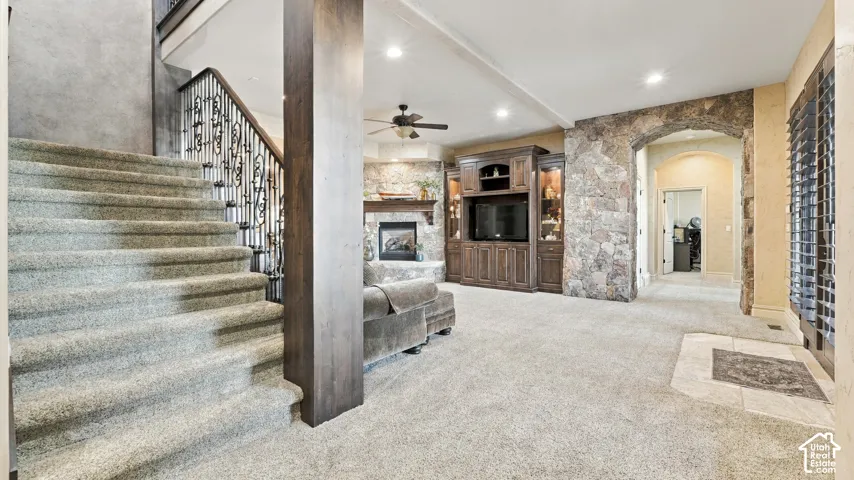 Staircase with iron balusters, floor-to-ceiling stone accent wall, custom built-in cabinetry, recessed lighting, and wood-finish support column