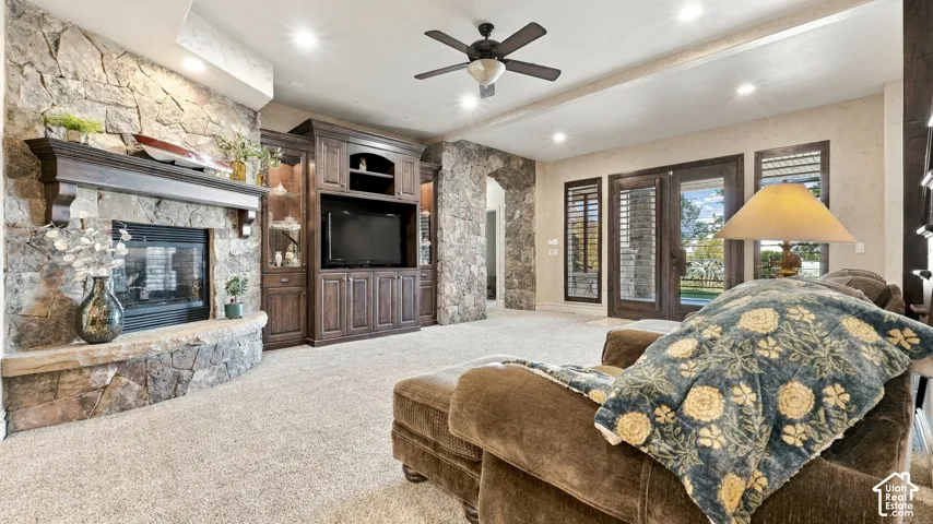 Floor-to-ceiling natural stone fireplace with a wood mantel, custom built-in wooden cabinetry, recessed lighting, ceiling fan, and double glass-paneled doors