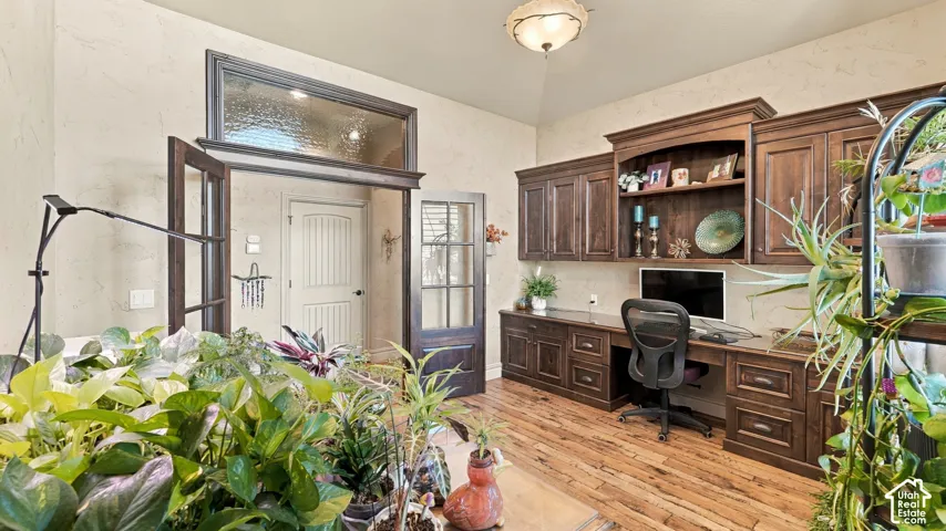Custom built-in wood cabinetry with integrated desk space, wood-finish flooring, French doors with glass panes, vaulted ceiling, and decorative glass transom window