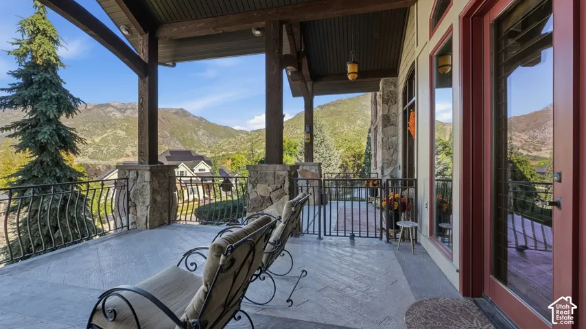 Covered patio featuring stone-clad support columns, herringbone-patterned stone flooring, decorative metal railings, and mountain scenery