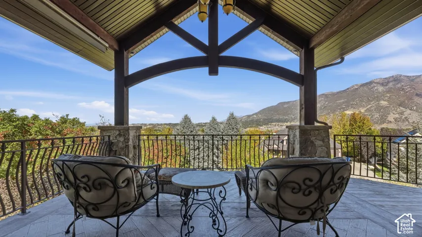 Covered patio featuring a vaulted timber-frame ceiling, stone-based columns, metal railings, and natural mountain scenery