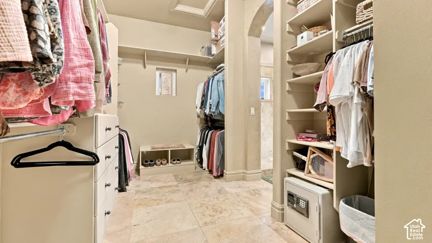 Walk-in closet featuring custom built-in cabinetry, floor-to-ceiling storage shelves, a dedicated shoe organizer, a built-in wall safe, and stone tile flooring