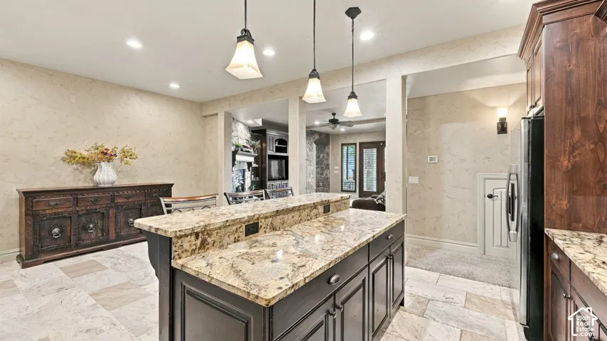 Kitchen featuring a dark-finish center island with stone countertop, tile flooring, recessed ceiling lighting, and three pendant lights