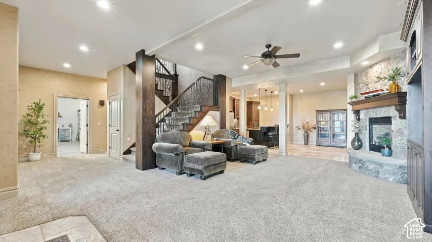 Open interior space featuring a stone-faced fireplace with a wood mantel, dark wood staircase with wrought iron balusters, recessed lighting, and built-in cabinetry