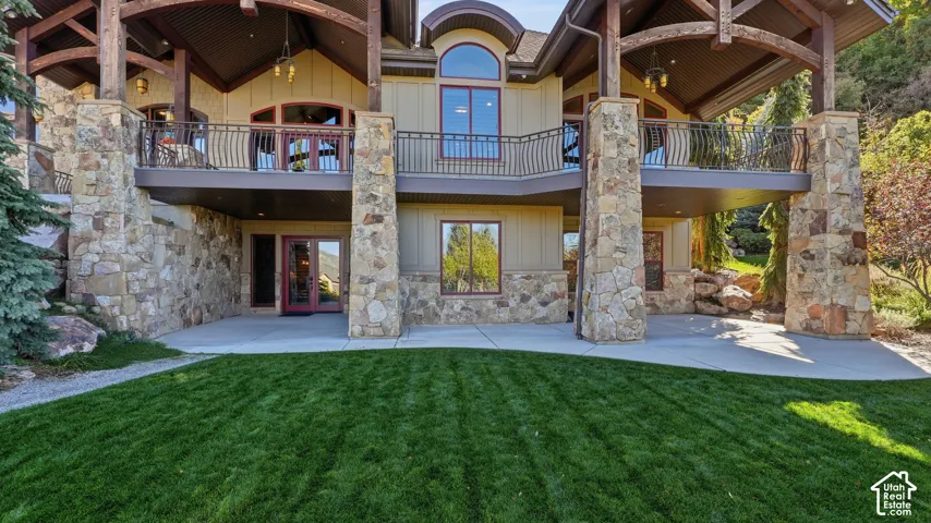 Custom-built exterior featuring stone masonry pillars, multi-level covered deck space, iron railings, expansive concrete patio, and board-and-batten siding