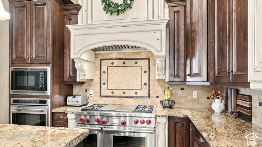 Custom cabinetry, stone countertops, professional-grade stainless steel range, built-in wall oven and microwave, and decorative tile backsplash with framed inlay