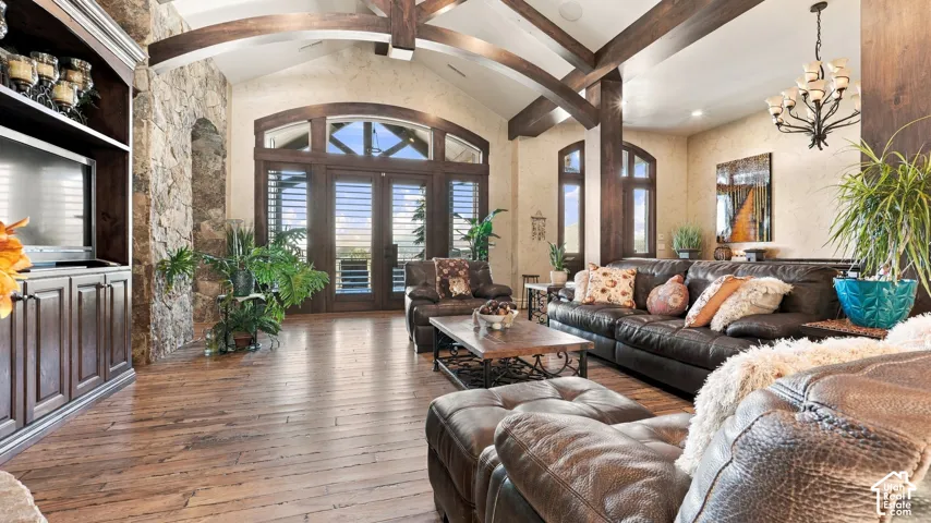 Vaulted ceiling with exposed wood-finish beams, stone-faced accent wall, wood-finish flooring, custom built-in cabinetry, and multi-pane arched doors