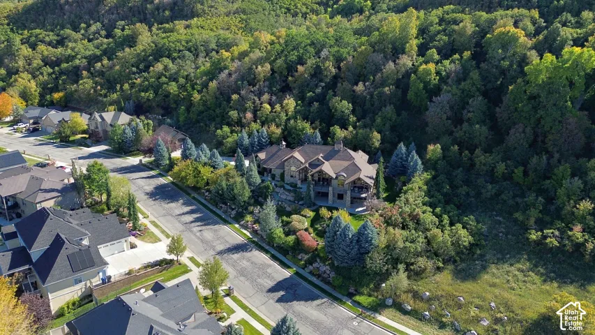 Multi-level residential structure featuring stone and shingle exterior siding, a multi-pitched roofline, integrated multi-story covered balconies, and landscaped grounds situated against a dense woodland backdrop