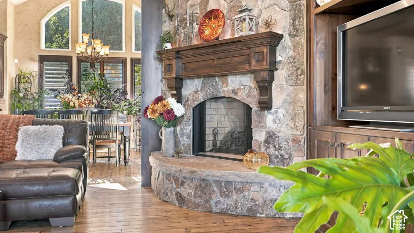 Floor-to-ceiling stone fireplace featuring a prominent wood mantel and raised stone hearth, wood-finish flooring, vaulted ceilings, and built-in wooden cabinetry