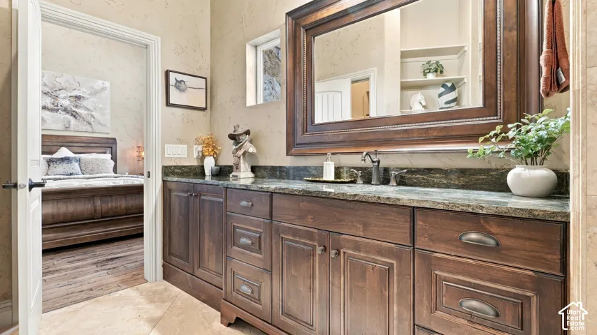 Custom dark wood cabinetry, slab countertop, built-in mirror with matching wood frame, and tile flooring