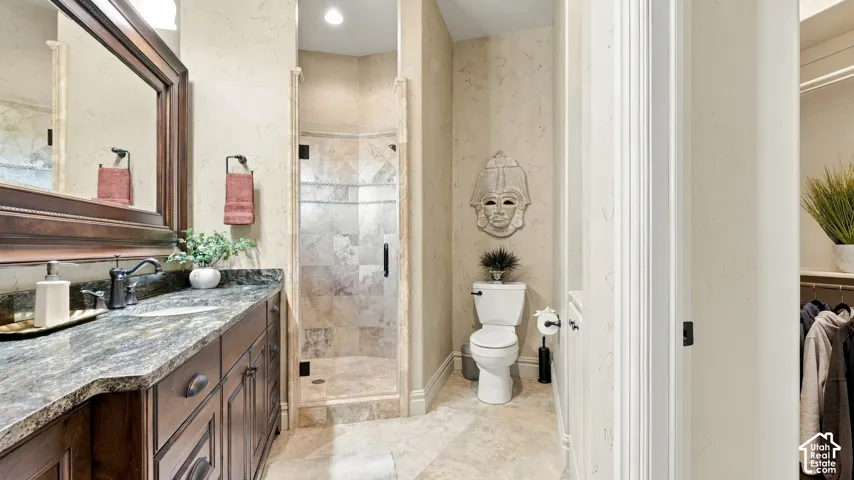 Custom vanity featuring stone-finish countertop with undermount sink, dark wood cabinetry, walk-in shower with stone tile surround, and tile flooring