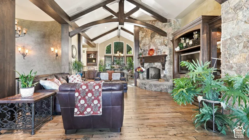 Vaulted ceiling with exposed timber trusses, stone fireplace with a carved wood mantel, built-in cabinetry, and wood-finish flooring