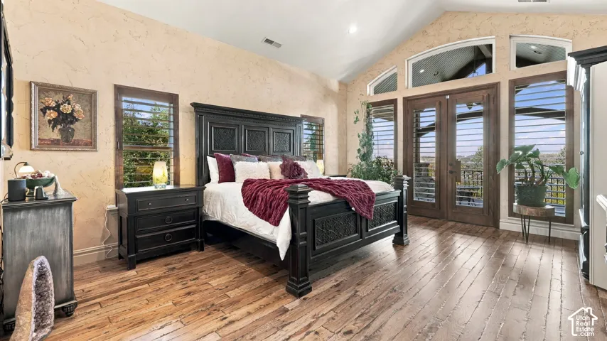 Vaulted ceiling, wood-finish flooring, textured wall finish, and double glass-paneled doors with arched transom windows