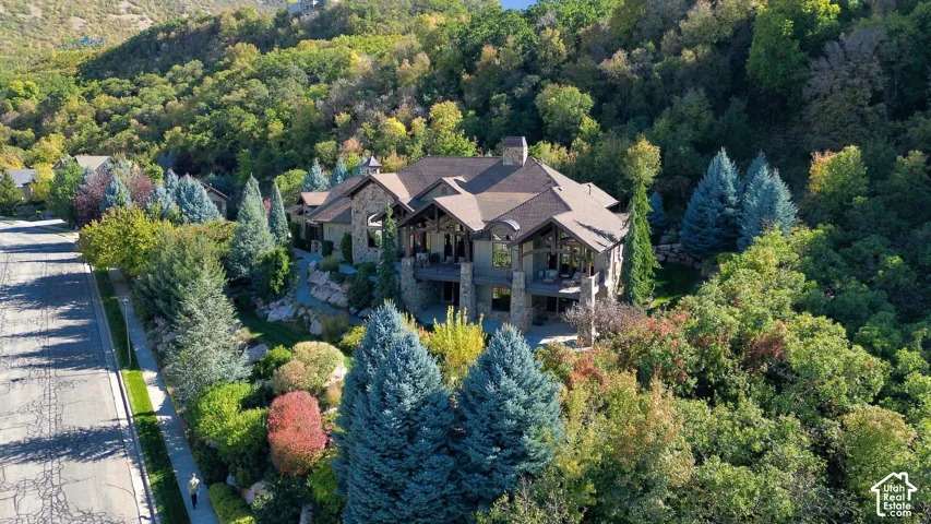 Multi-level residence featuring stone masonry exterior, timber framing accents, expansive covered balconies, and steeply pitched roofline situated on a heavily wooded lot