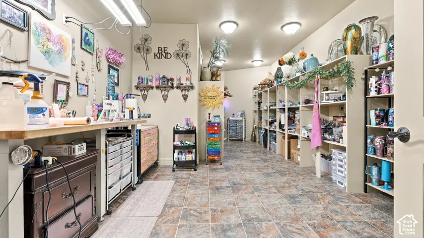 Utility room featuring stone-tile flooring, extensive built-in floor-to-ceiling shelving, fixed wall-mounted work surfaces, and overhead flush-mount lighting