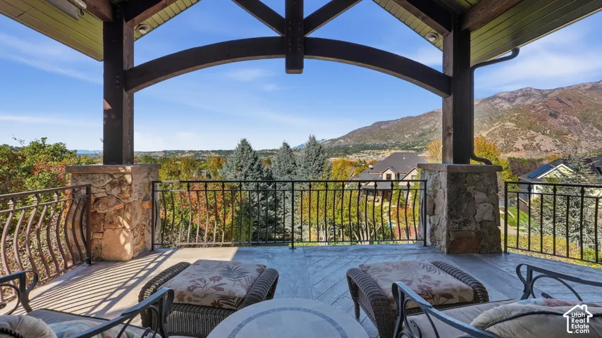 Covered stone patio featuring timber-framed overhead beams, stone-clad support pillars, wrought iron railings, and mountain scenery