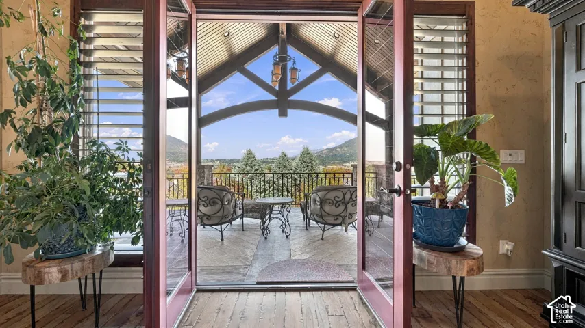 Double French doors opening to a covered balcony with a vaulted timber-truss ceiling, pendant lighting, and metal railing