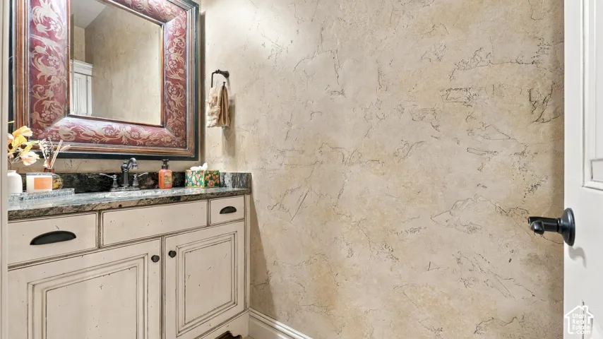 Distressed-finish cabinetry with stone-surface countertop, textured wall treatment, and wall-mounted towel hardware