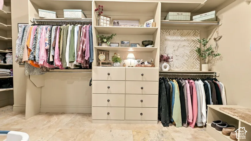Custom walk-in closet featuring extensive built-in cabinetry, eight integrated storage drawers, multiple hanging rods, and stone-finish flooring