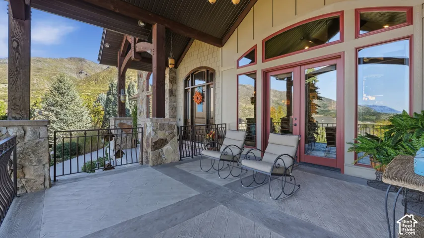 Covered patio featuring stone-clad pillars, stamped concrete flooring, exposed timber support beams, and mountain scenery