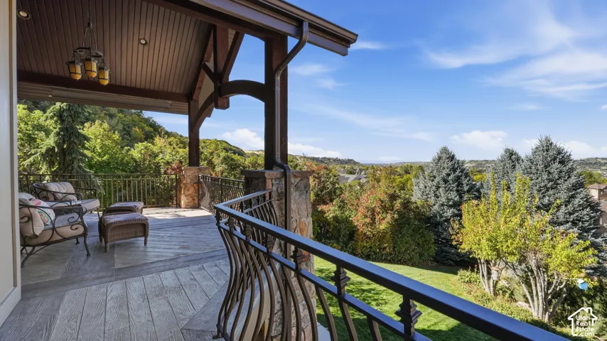 Covered terrace featuring wood-finish tile flooring, stone-clad pillar supports, decorative metal railing, and recessed ceiling lighting
