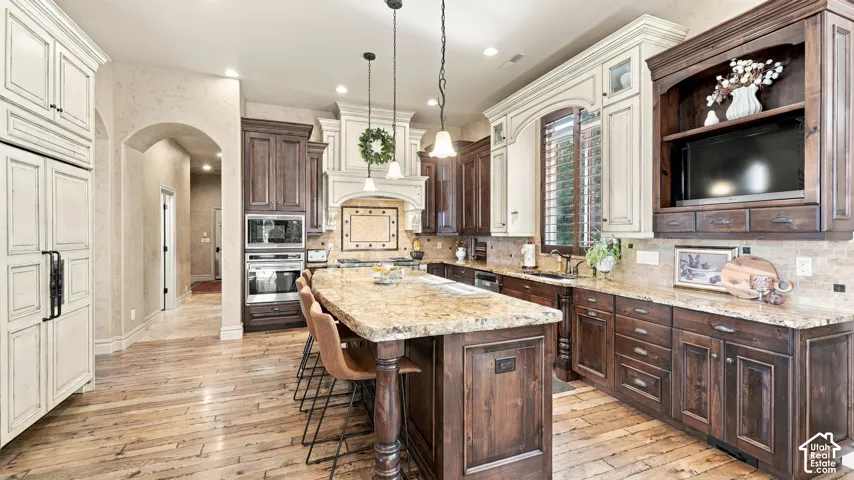 Kitchen featuring two-tone custom cabinetry, a large central island with stone countertop, built-in double wall ovens, wood-finish flooring, and decorative pendant lighting