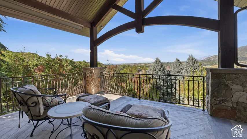 Covered deck featuring wood-finish tile flooring, exposed timber trusses, stone pillars, and metal railing
