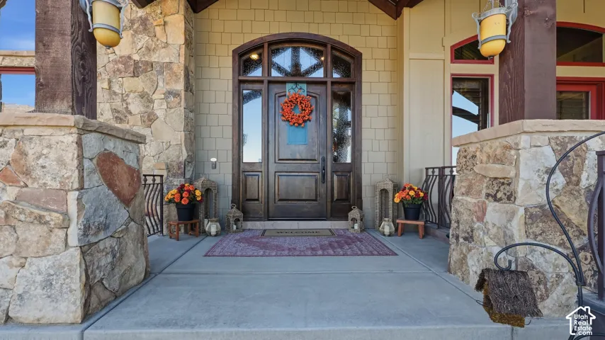 Covered entrance featuring stacked stone pillars, shingle siding, a wood door with an arched transom window, and mounted exterior lanterns