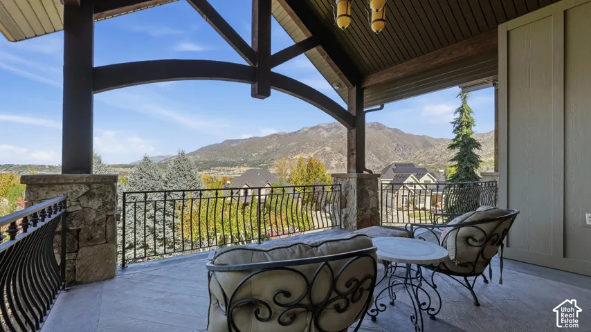 Covered balcony featuring exposed timber trusses, stone-clad pillars, wrought iron railings, and mountain backdrop