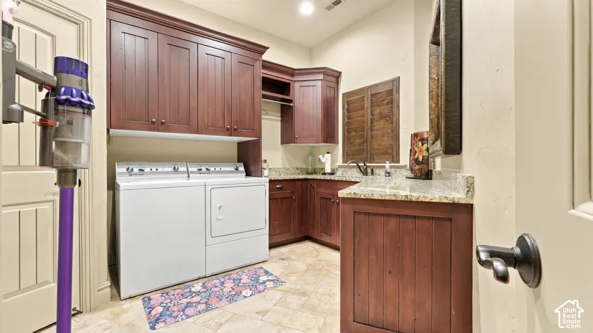 Laundry room featuring dark wood-finish cabinetry, stone-surfaced countertops, a built-in sink with a matte black faucet, and stone-tiled flooring