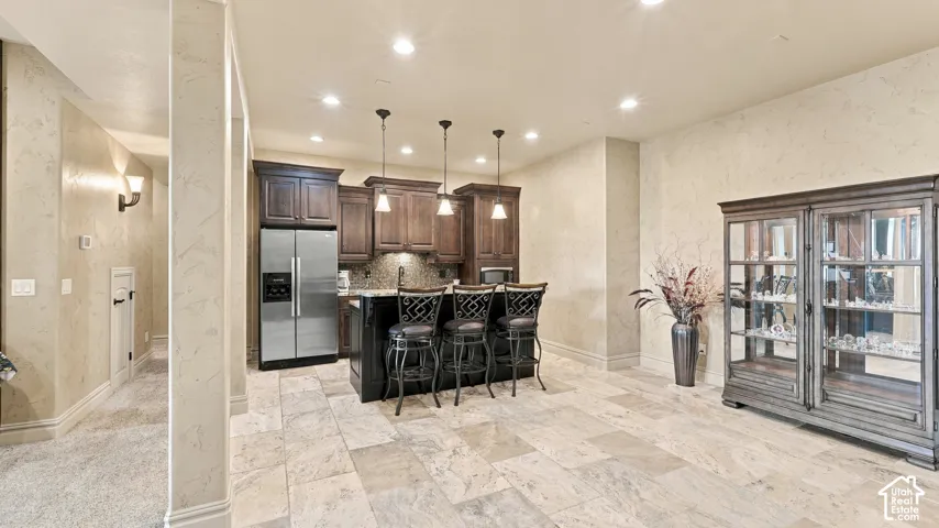 Kitchen featuring dark wood cabinetry, a stone-topped island, stainless steel refrigerator, stone tile flooring, and three pendant lights