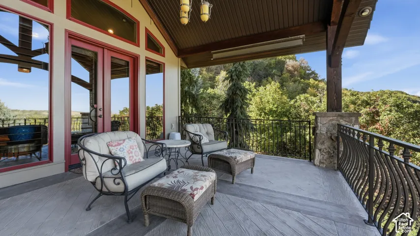 Covered outdoor terrace featuring stone-pillar supports, decorative metal railing, wood-finish flooring, and expansive windows