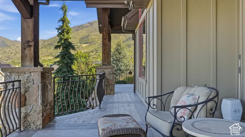 Covered patio featuring stone-clad pillars, timber beam supports, metal railings, and mountain terrain backdrop
