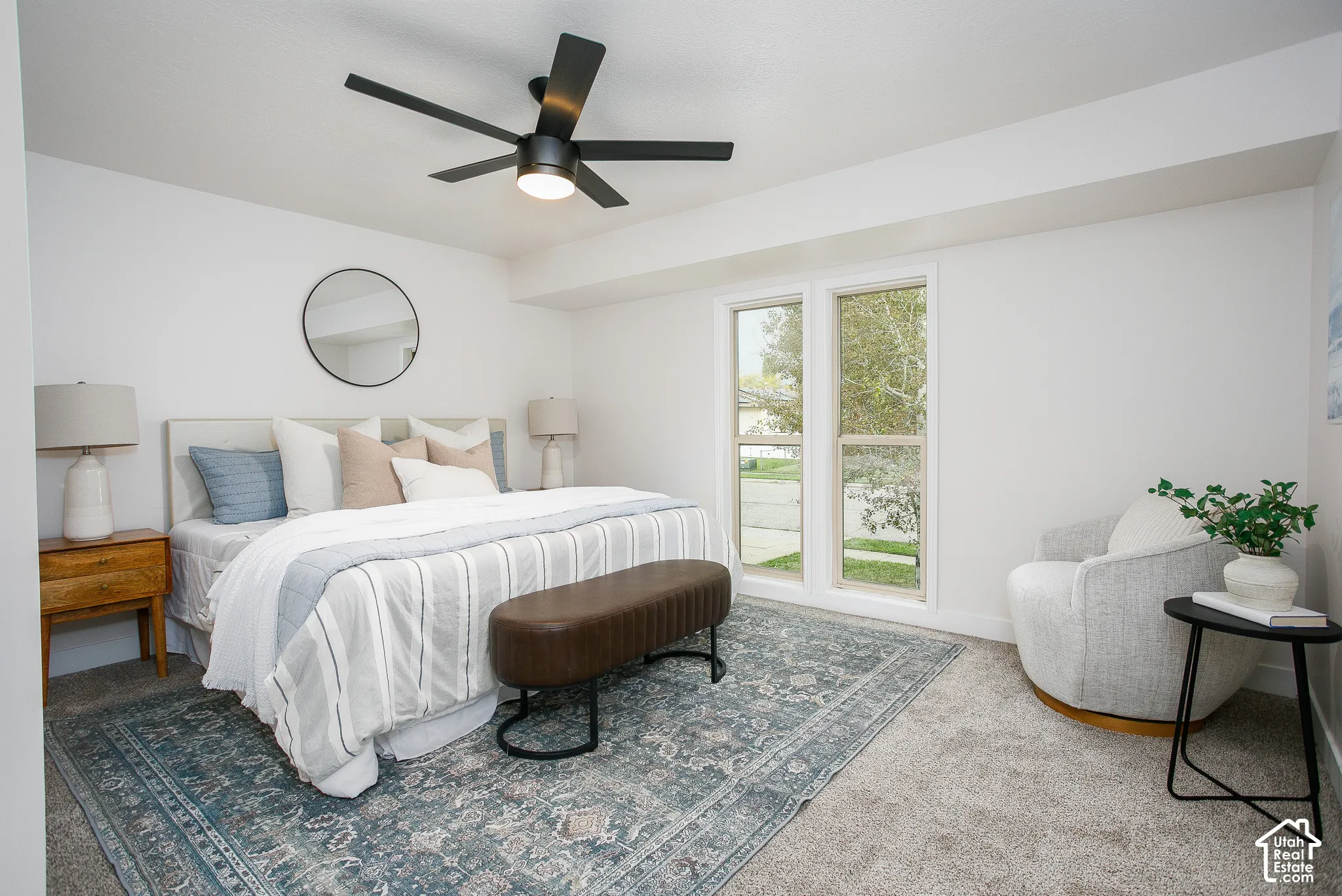 Neutral-toned interior space featuring recessed tray ceiling, matte black five-blade ceiling fan with integrated lighting, wall-to-wall carpeting, and dual-pane vertical windows
