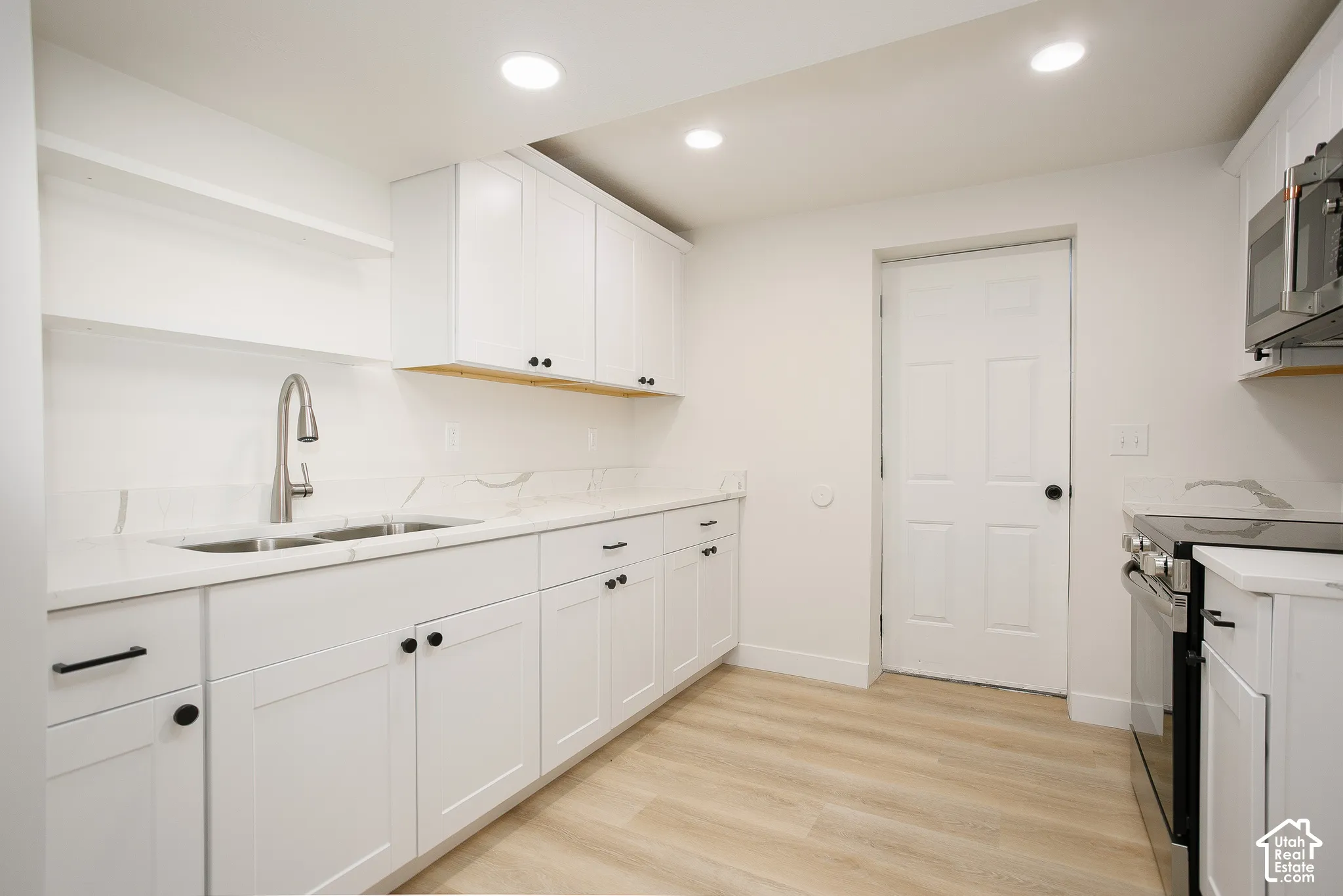 Kitchen featuring white shaker-style cabinetry, stone-finish countertops, stainless steel appliances, a pull-down faucet, and wood-finish flooring