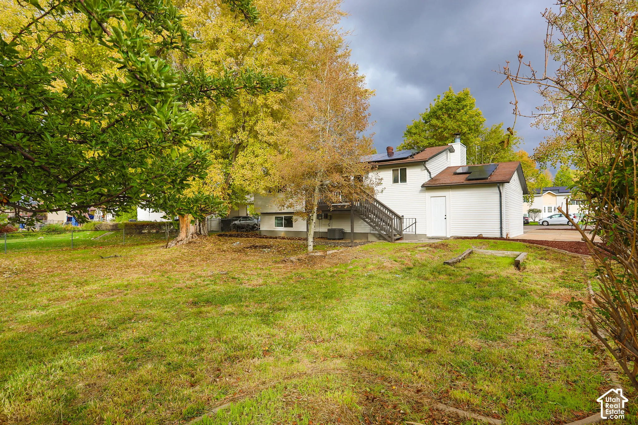 Exterior featuring light-colored siding, rooftop solar panels, a wooden staircase, and mature trees on the grounds
