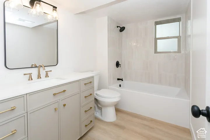 Bathroom featuring a custom vanity with a light-toned finish, quartz countertop, brass-tone hardware, a rectangular vanity mirror with matte black framing, and a tiled tub-shower surround with matte black fixtures