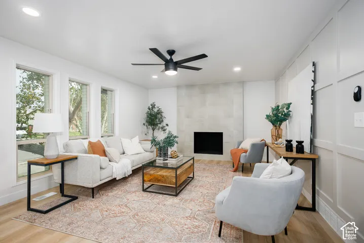 Living area featuring wood-finish flooring, a fireplace with large-format tile surround, board-and-batten wall detailing, recessed lighting, and a modern ceiling fan
