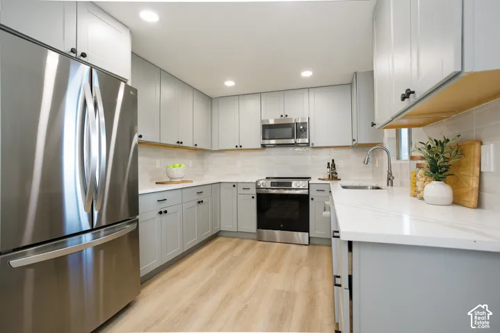 Kitchen featuring light gray shaker-style cabinetry, quartz countertops, stainless steel appliances, tile backsplash, and wood-finish flooring