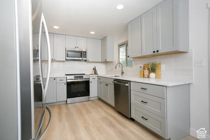 Kitchen featuring shaker-style grey cabinetry, stainless steel appliances, white stone-finish countertops, subway tile backsplash, and wood-finish flooring