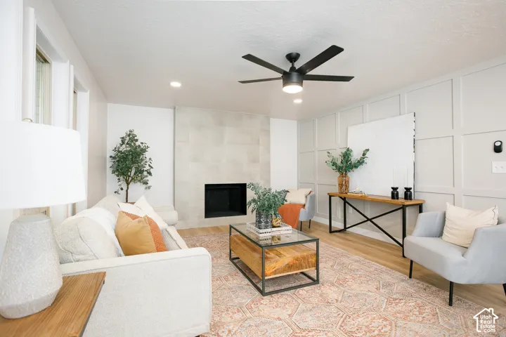 Living area featuring a fireplace with large-format tile surround, wall molding, wood-finish flooring, and a matte black ceiling fan
